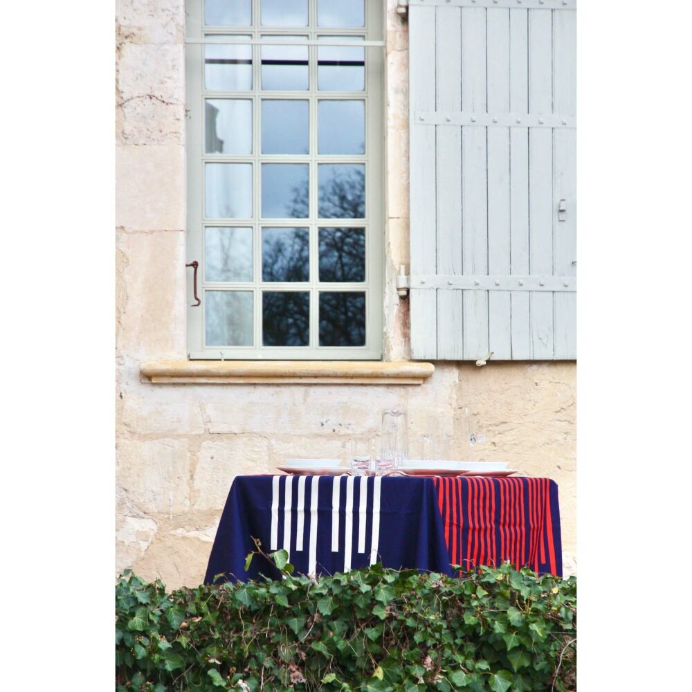 scene avec une nappe bleu marine et rayures rouges et blanches devant maison en pierre